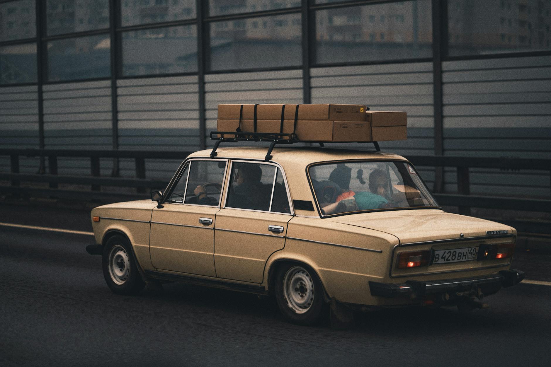 Jasny klasyczny sedan z bagażem na dachu jedzie autostradą obok miasta Jasny klasyczny sedan z bagażem na dachu jedzie autostradą obok miasta