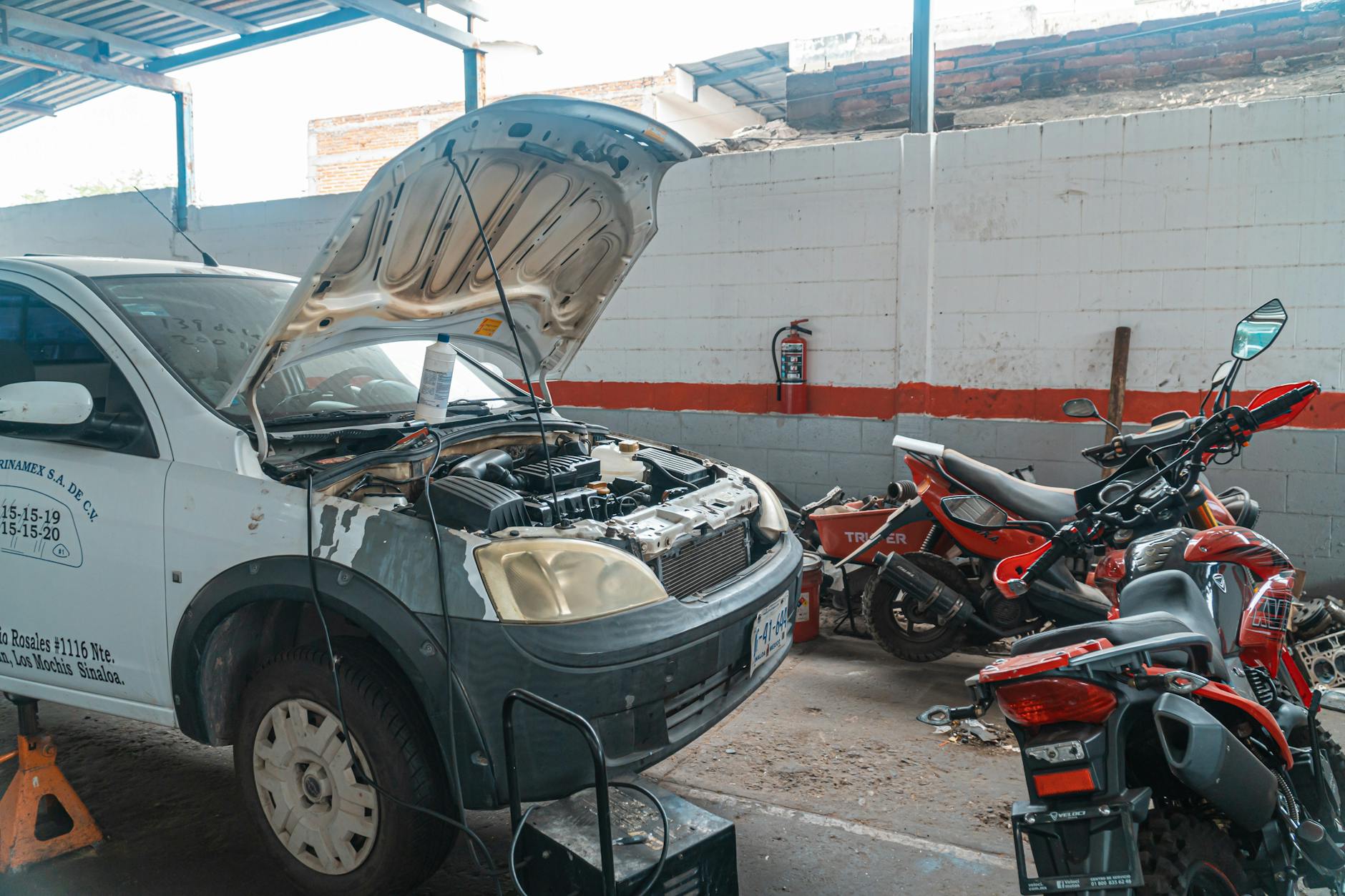 Samochód naprawiany w garażu obok motocykli i narzędzi