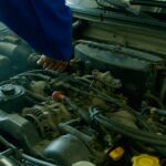 Mechanik w niebieskim kombinezonie naprawia silnik Aston Martina w garażu