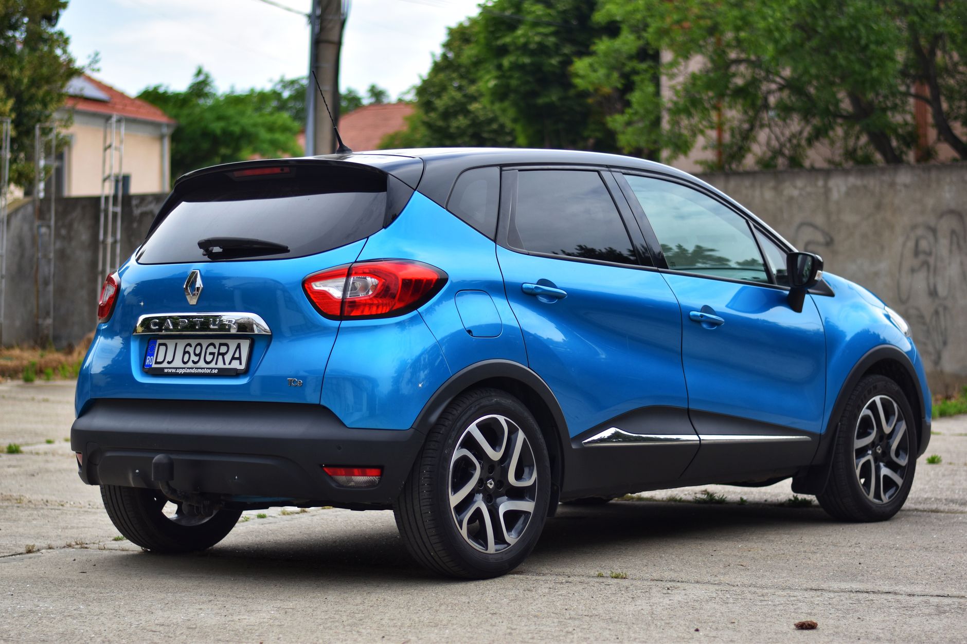 Niebieski Renault Captur zaparkowany przy zieleni na parkingu