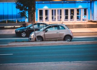 Mitsubishi Space Star jako miejskie auto z importu czy to się w ogóle opłaca Fiat 500 jedzie nocą obok nowoczesnego, niebiesko podświetlonego budynku
